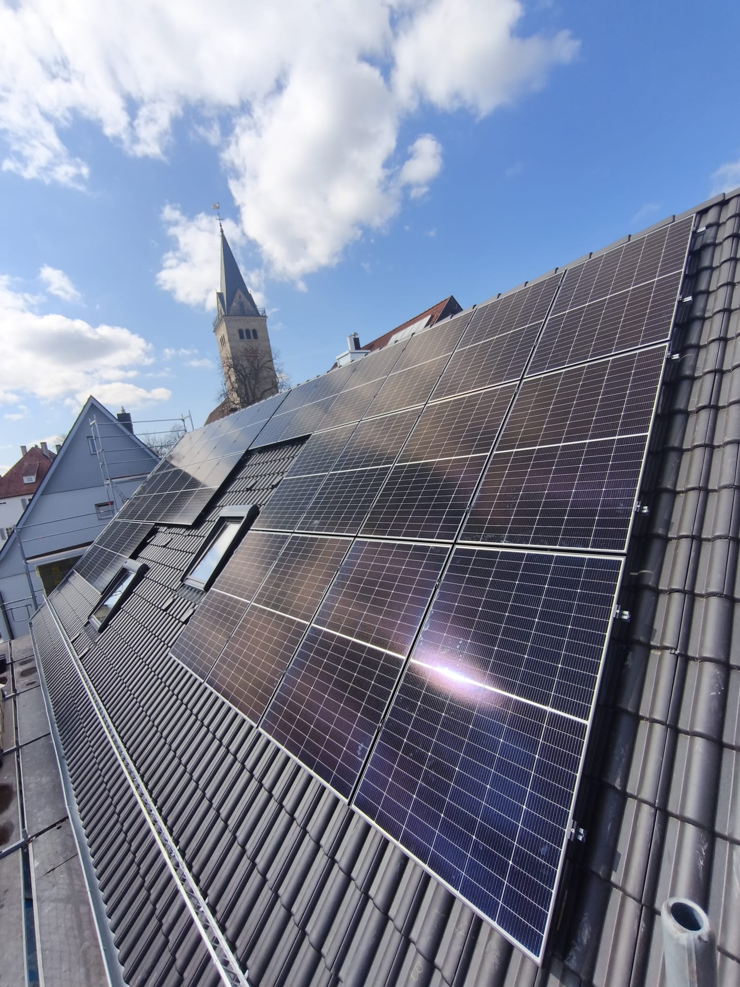 Photovoltaikanlage auf einem Ziegeldach mit Blick auf einen Kirchturm im Hintergrund
