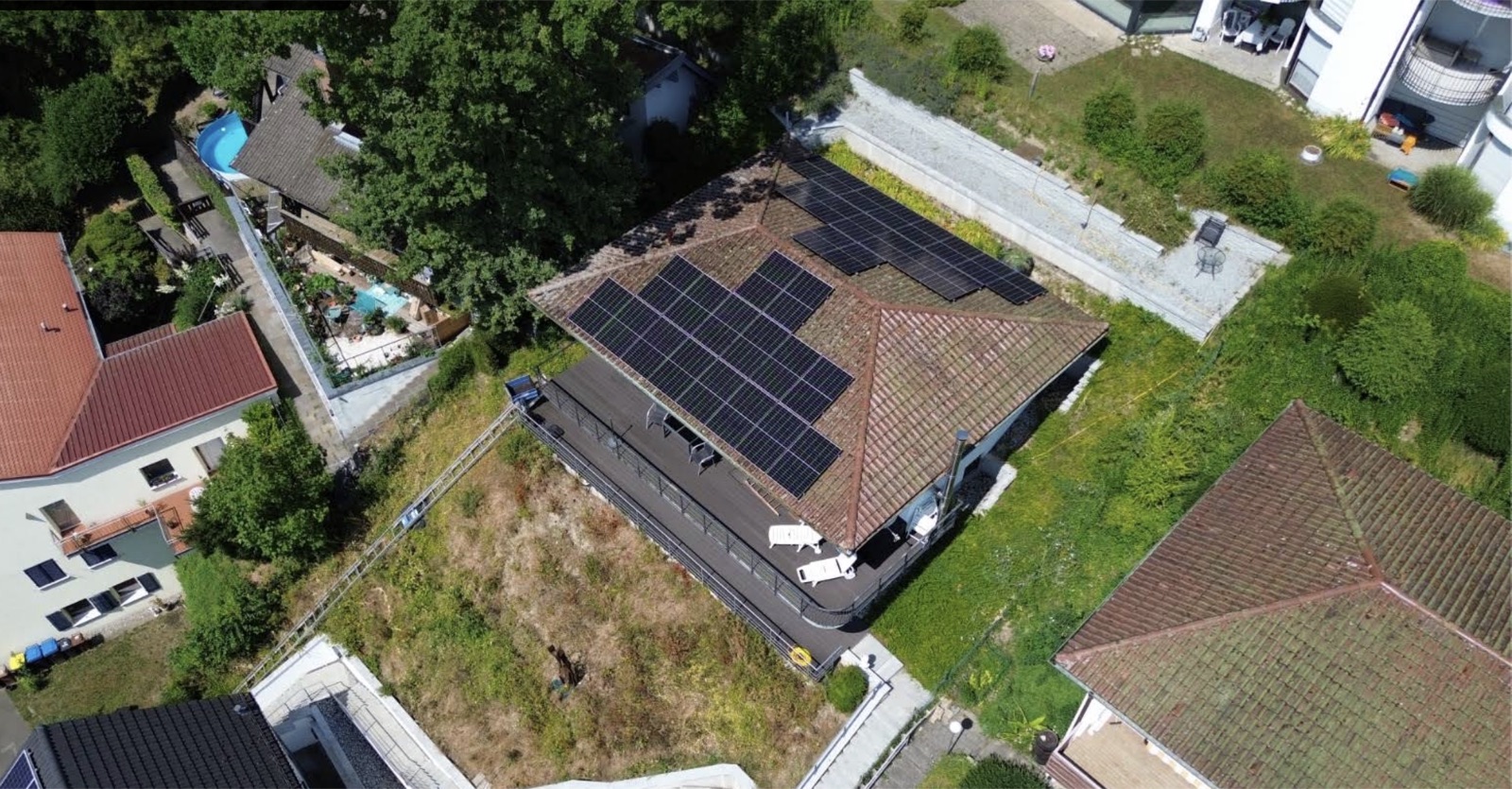 Luftaufnahme eines Hausdachs mit Photovoltaikanlage und Garten mit Pool