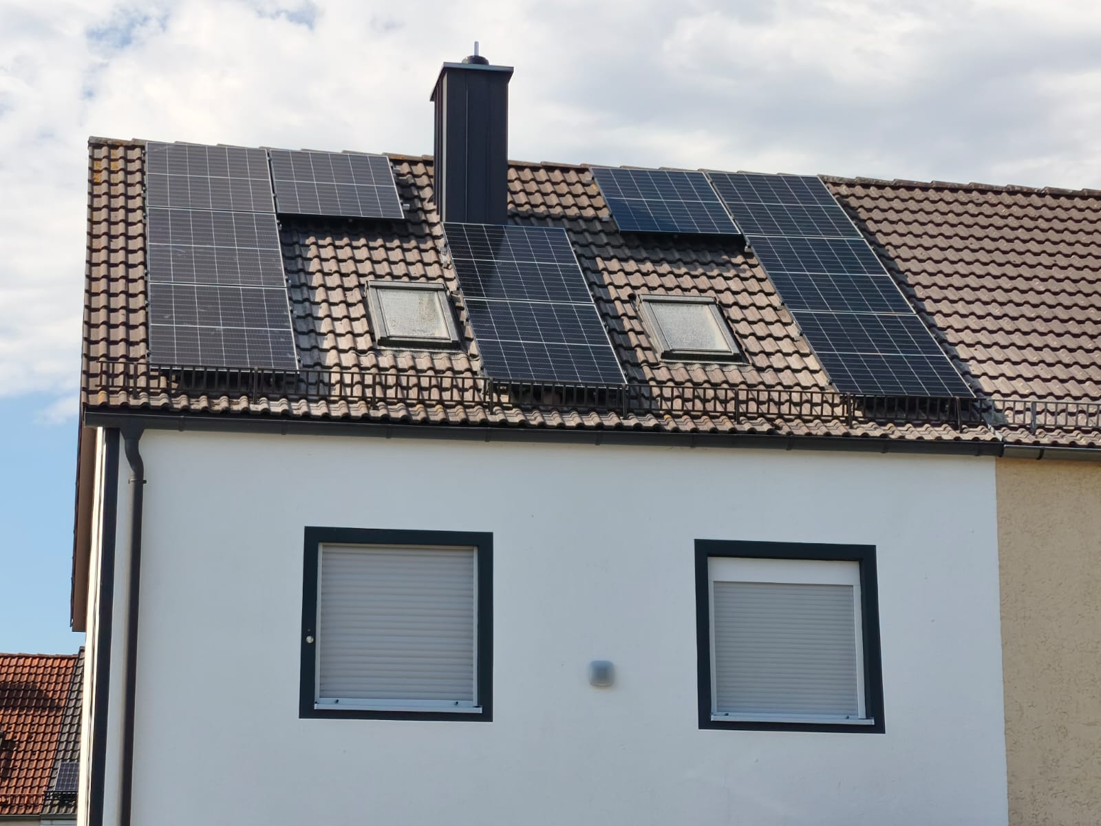 Photovoltaikanlage auf einem Ziegeldach, um Dachfenster und Schornstein herum verlegt