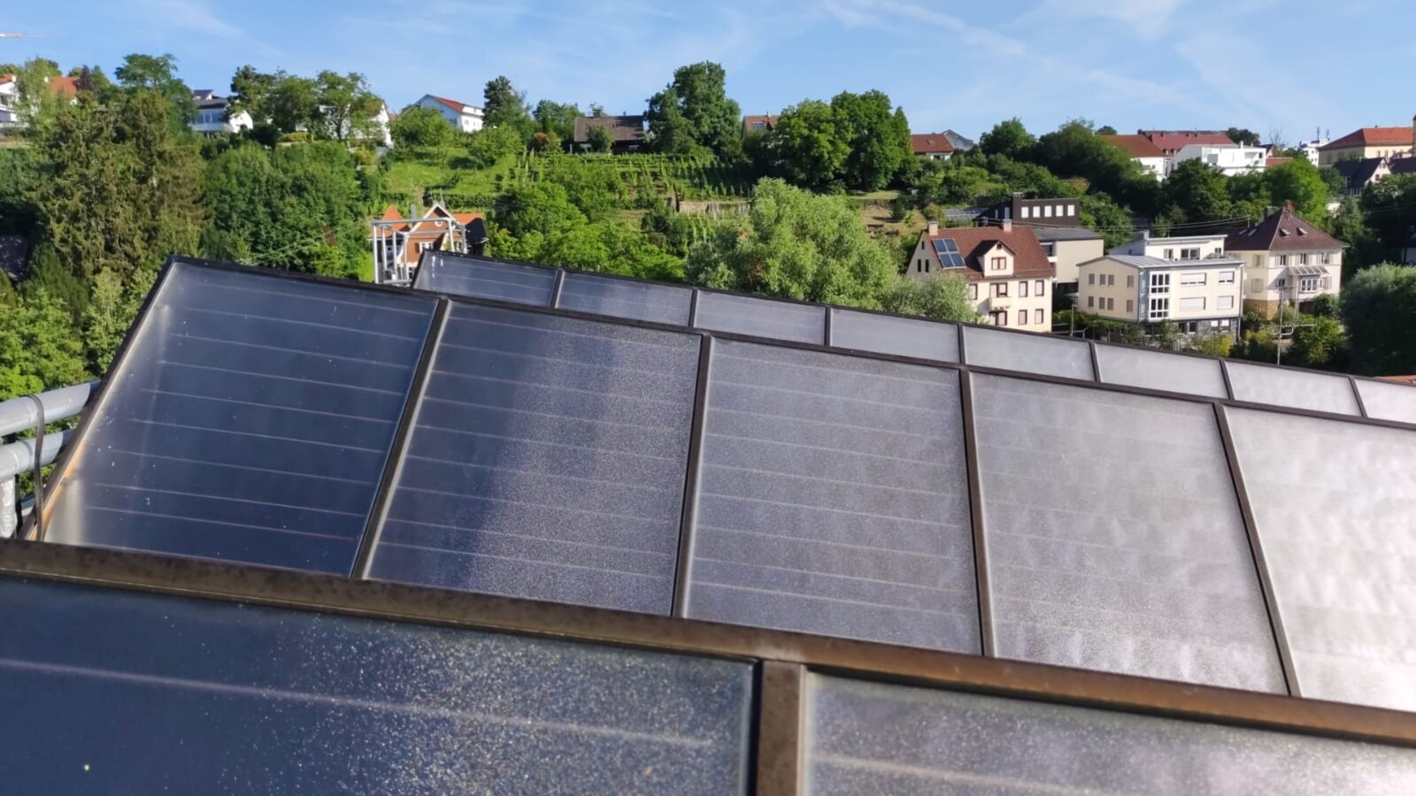 Solarthermie-Kollektoren auf einem Dach mit Blick auf einen bewaldeten Hügel im Hintergrund