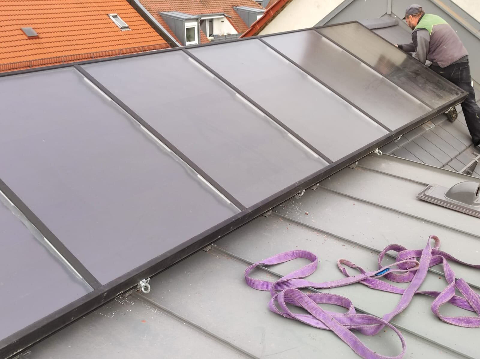 Monteur bei der Montage eines Solarthermie-Kollektors auf einem Dach